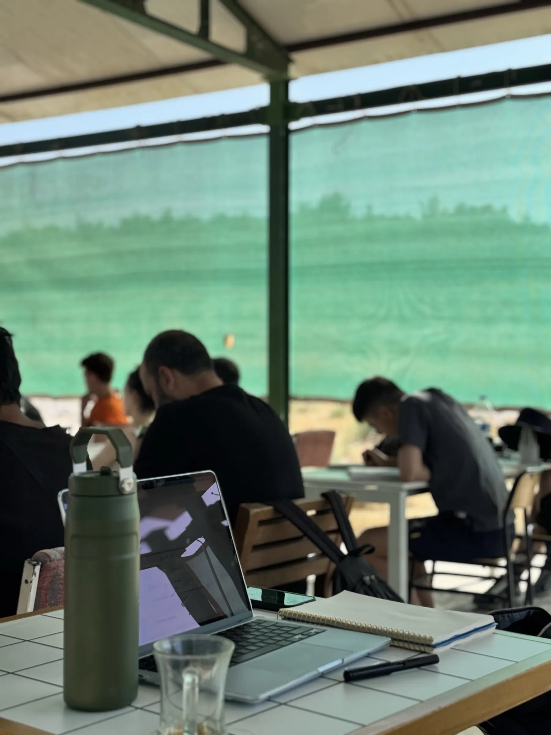 Participants working at tables under the canopy at Bilimler Köyü